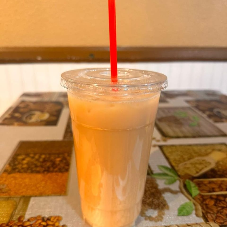 Iced peach-colored drink with a red straw in a clear plastic cup on a patterned tablecloth.