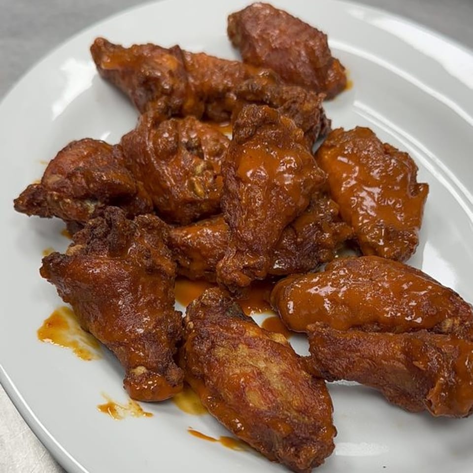 A white plate piled high with Gina's Pizzeria's crispy, saucy buffalo chicken wings.