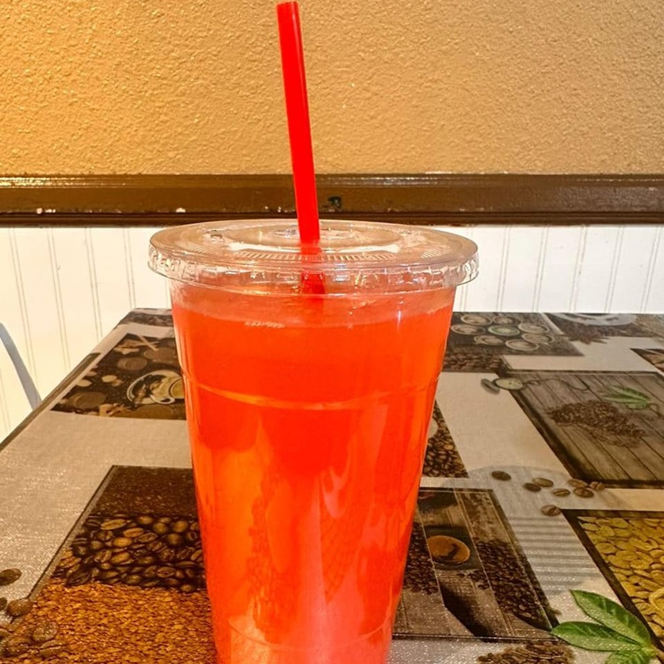 A clear plastic cup of red drink with a red straw sits on a coffee-themed tablecloth.