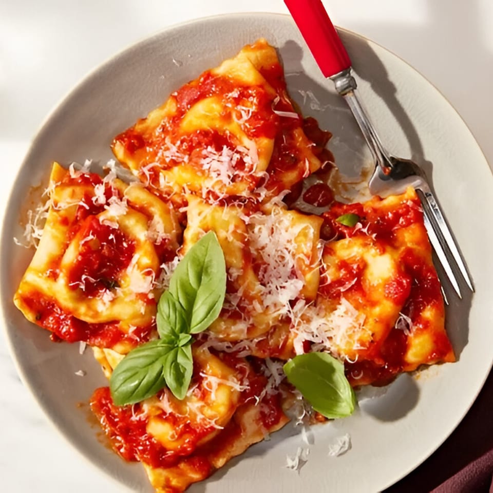 Plate of ravioli with red sauce, grated cheese, and fresh basil, with a red-handled fork.